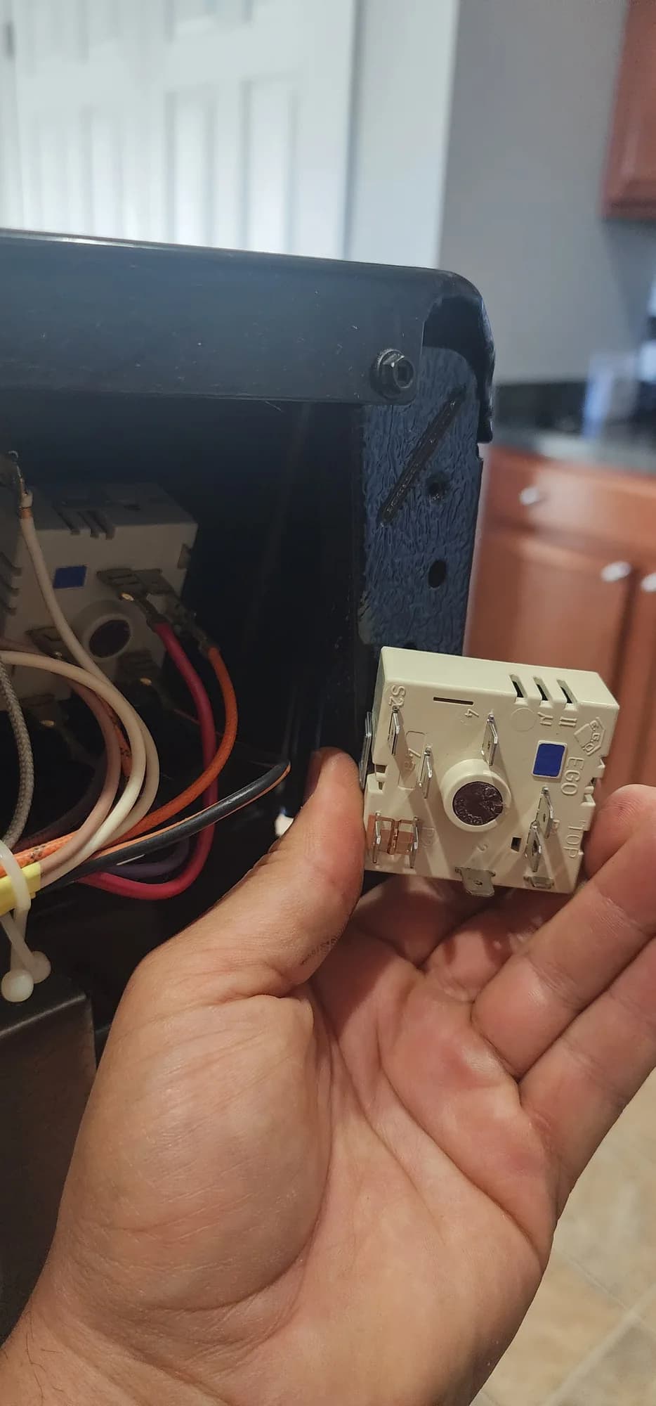 Burner control switch held beside the open control panel of the Frigidaire range